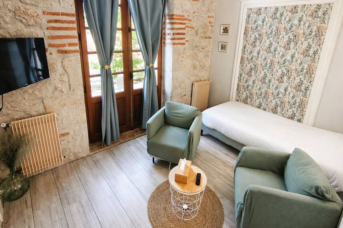 A room with a bed, two sofas, a TV, and a window with curtains.