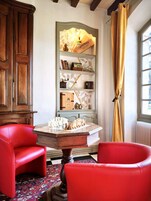 Una habitación con un tablero de ajedrez, sillas rojas, un aparador de madera y una estantería con diversos objetos.
