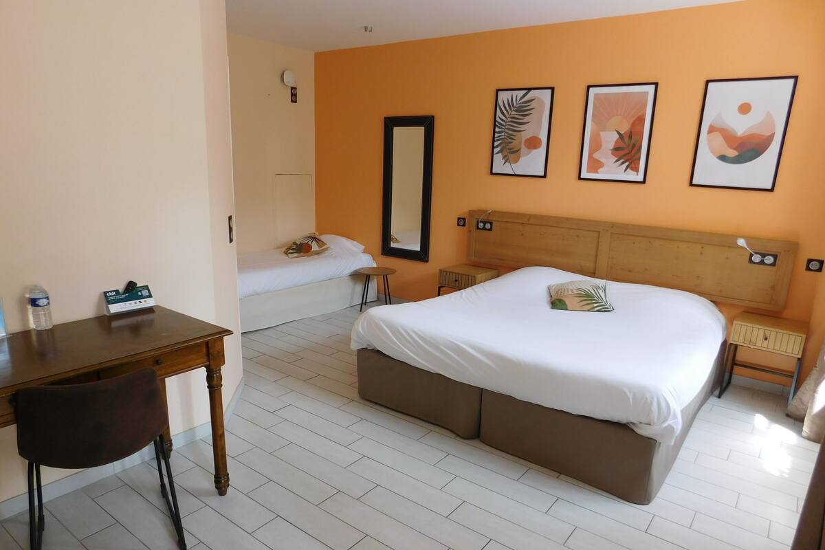 A hotel room with a bed, a desk, a chair, a small table, and a nightstand.
