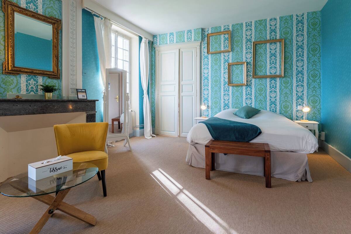 A bedroom with a bed, bedside table, chair, and a glass table with a box.