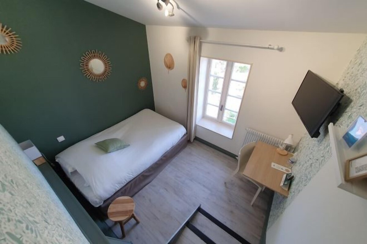 A compact room with a bed, a small desk, a chair, a radiator, and a television mounted on the wall.