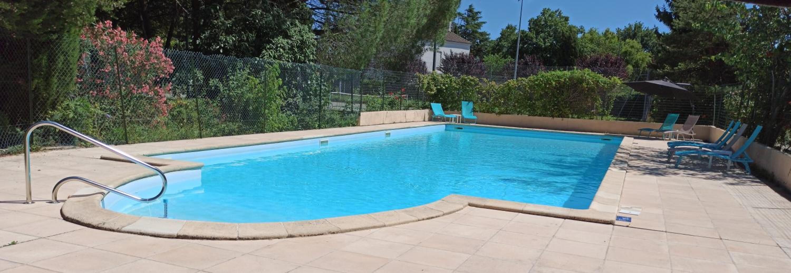 Une piscine rectangulaire avec un escalier en métal sur un de ses côtés, entourée d’une terrasse carrelée.