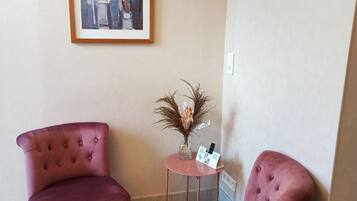Een kamer met twee comfortabele fauteuils, een kleine tafel met een vaas en een afstandsbediening, en een lijst met een schilderij aan de muur.