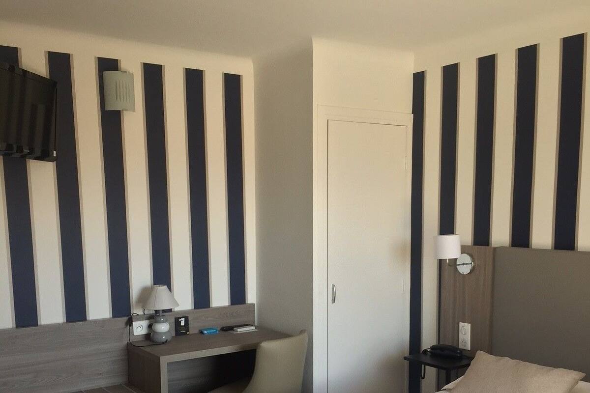 A hotel room with a bed, a desk, a chair, a nightstand, and a lamp.