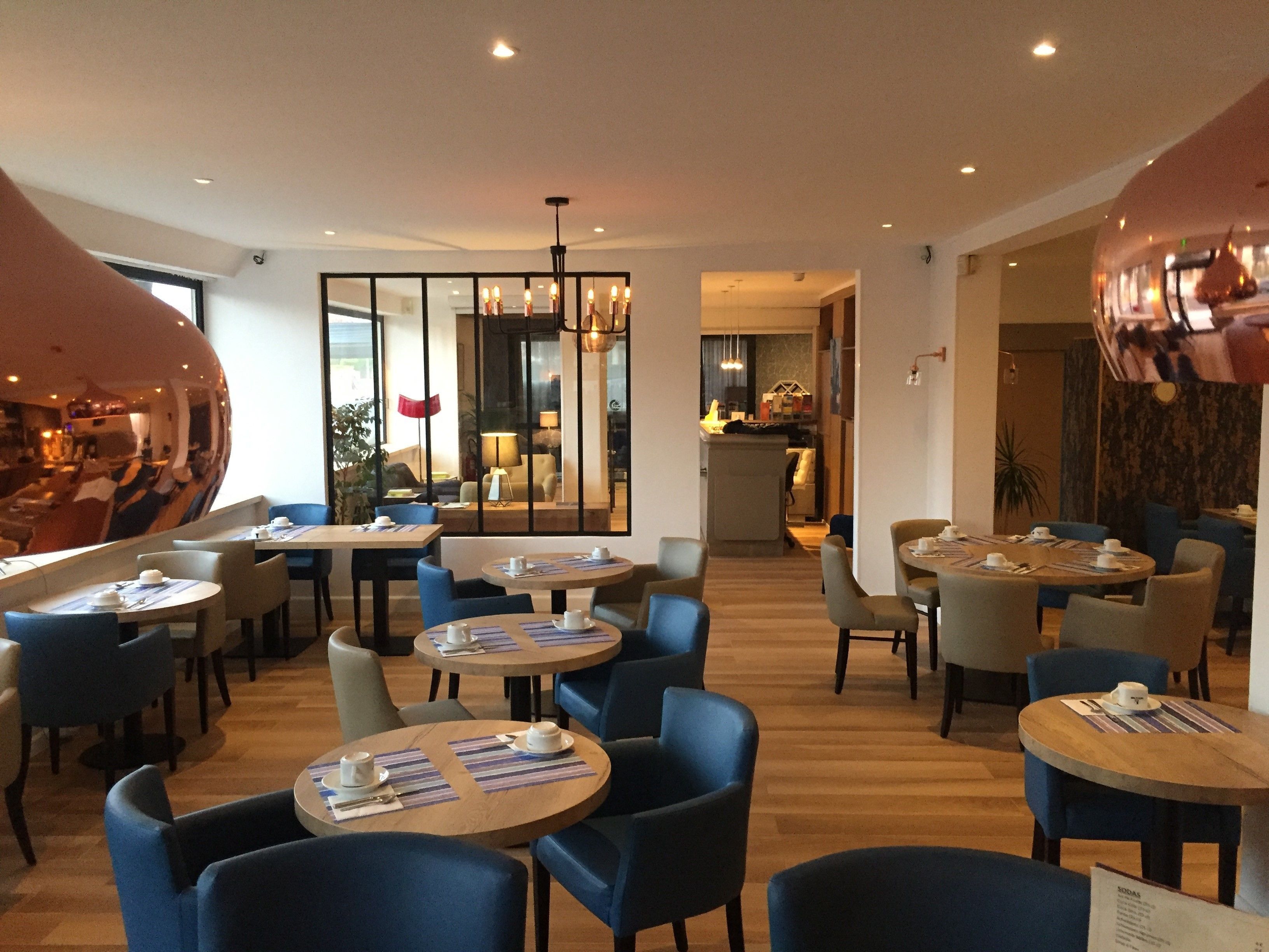 Un moderno vestíbulo de hotel con mesas redondas, sillas azules y un gran espejo esférico.