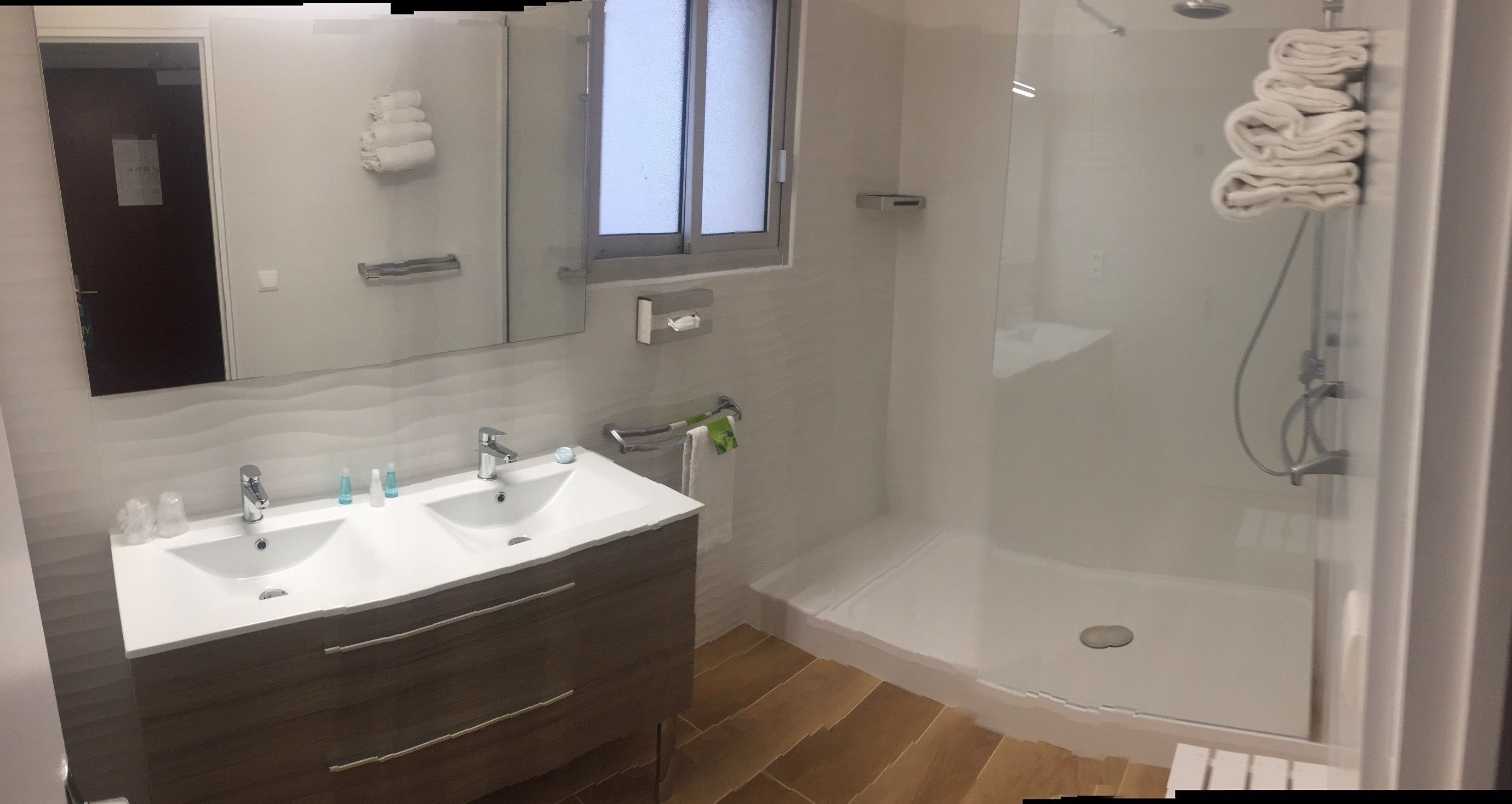 A bathroom with two sinks, a mirror, a towel rack, and a glass-enclosed shower.