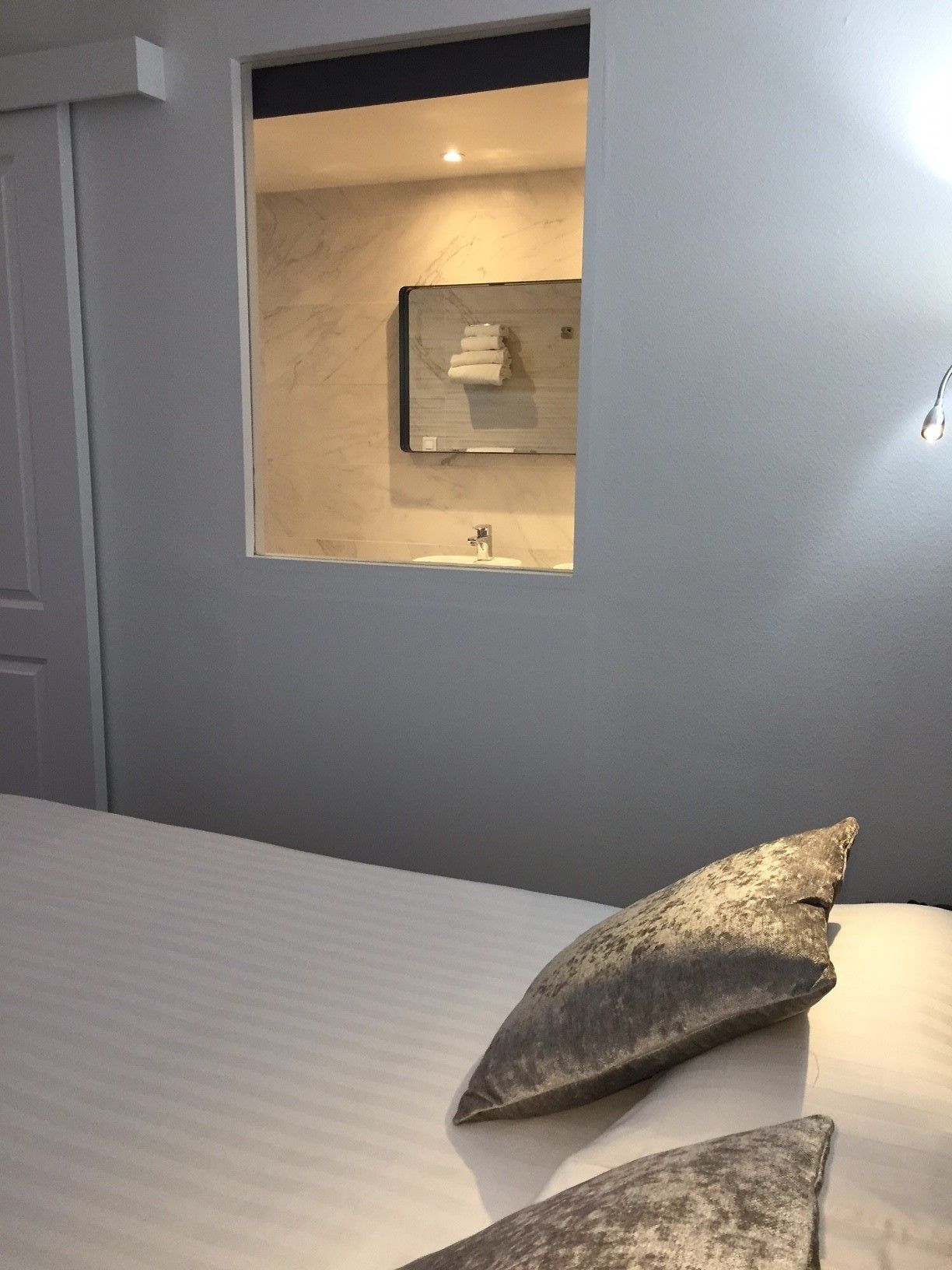 Une chambre à coucher avec un lit, des oreillers, une petite fenêtre avec un miroir et un lavabo.