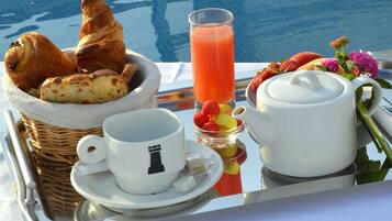 Bandeja de café da manhã com croissants, um copo de suco de laranja, um bule, uma xícara e uma pequena tigela de frutas à beira de uma piscina.