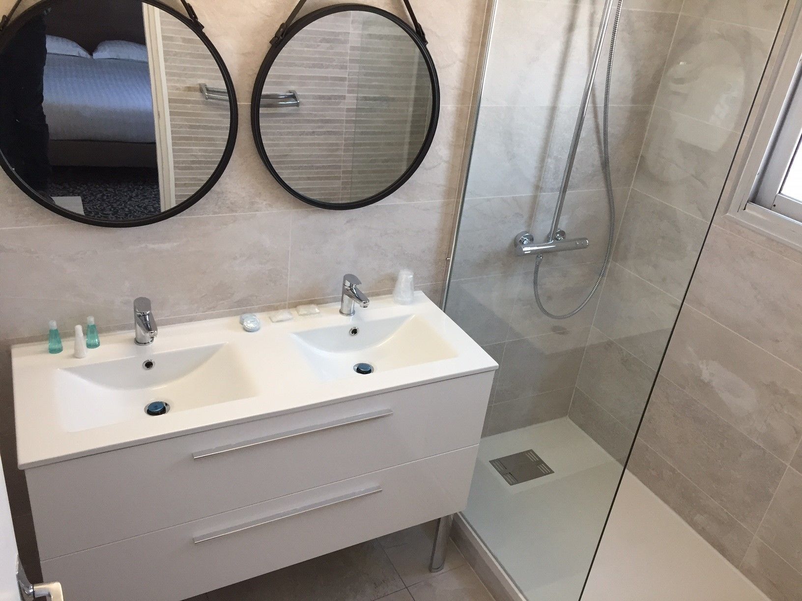 Une salle de bain avec deux vasques, deux miroirs, une douche et un espace douche fermé par des parois de verre.