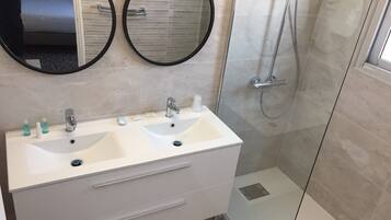 Une salle de bain avec deux vasques, deux miroirs, une douche et un espace douche fermé par des parois de verre.