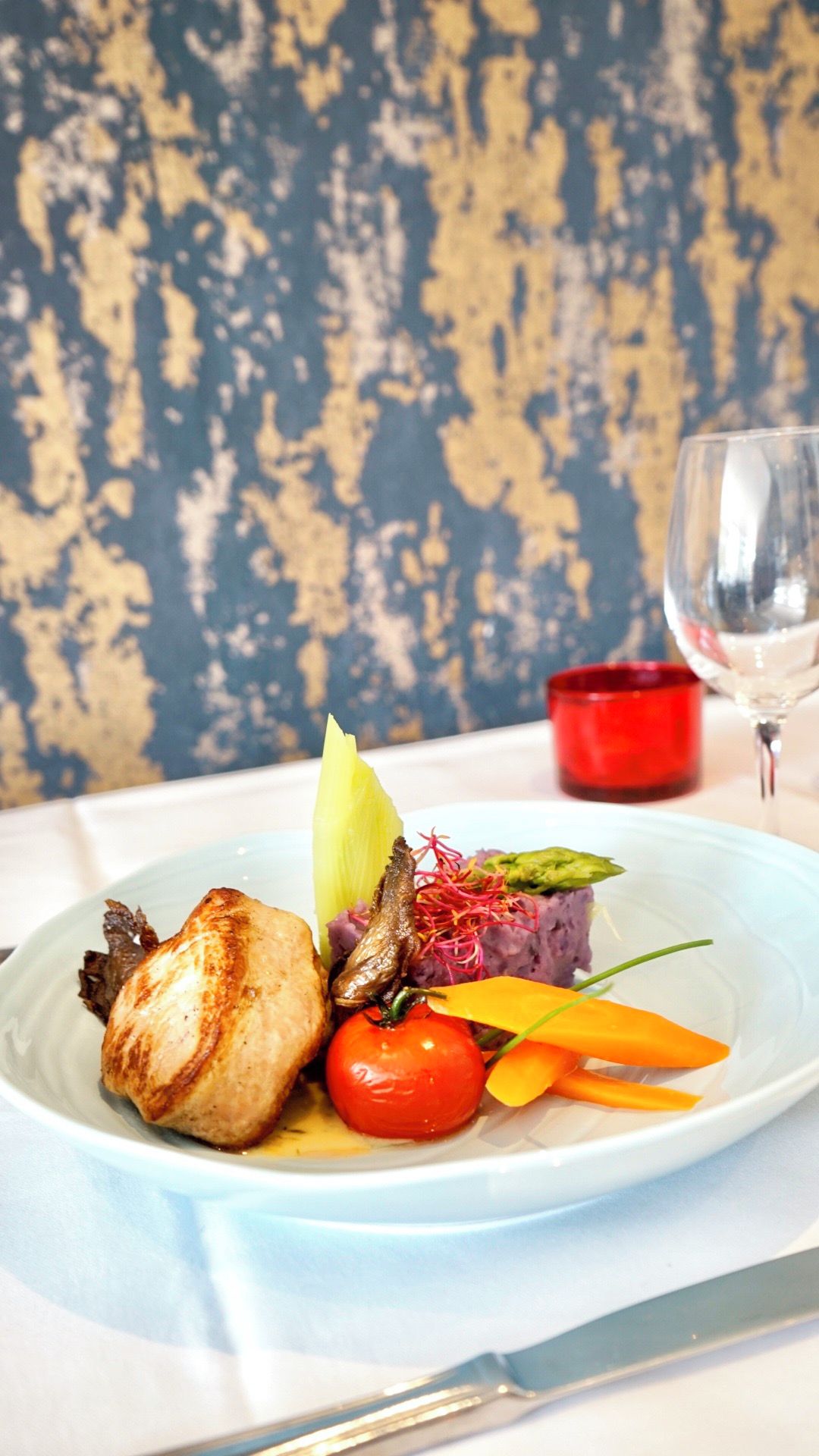 A plate of food with a glass of wine and a red candle on a table.