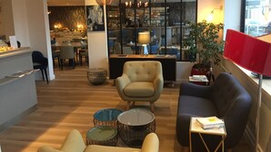 A modern living room with a sofa, armchairs, and a coffee table. There is a dining area in the background with a bar and kitchen. - Logis Hotel et Restaurant Le Galion Canet Plage (Canet-en-Roussillon)