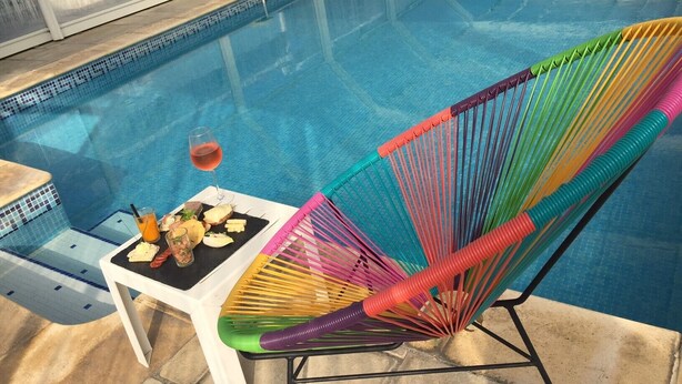 A poolside chair with a colorful woven design, a glass of red wine, and a plate with food and a drink. - Logis Hotel et Restaurant Le Galion Canet Plage (Canet-en-Roussillon)
