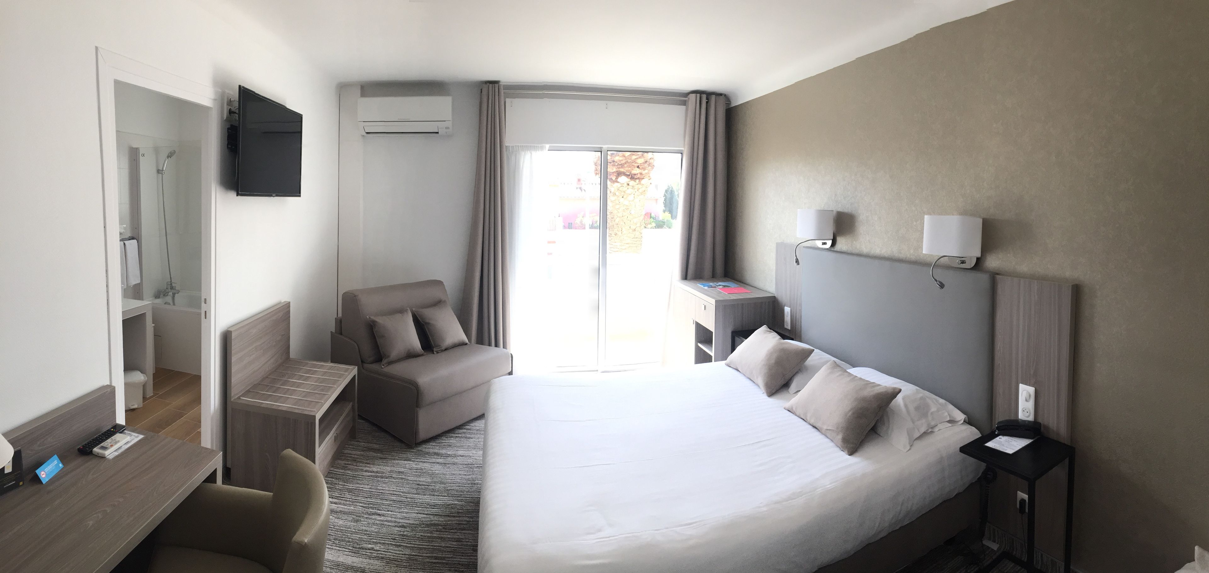 A hotel room with a bed, a desk, a chair, a TV, and a bathroom.