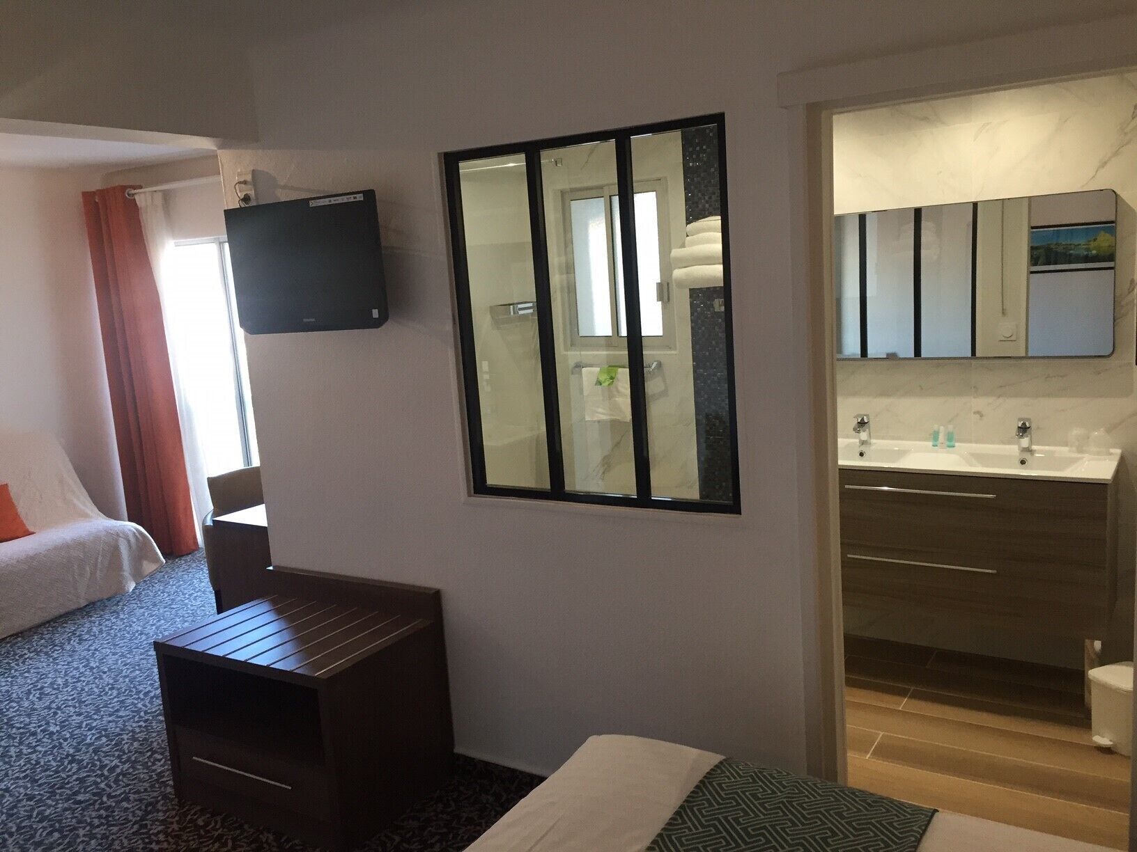 Ein Hotelzimmer mit Bett, Schreibtisch, Fernseher, einem großen Spiegel und einem Badezimmer mit Waschbecken und Toilette.