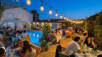 An outdoor dining area with tables and chairs, a pool, and string lights.