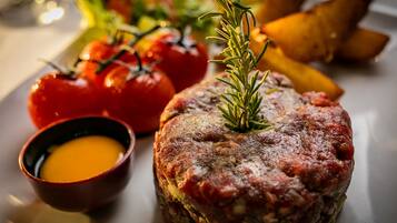 Tartar de carne con una ramita de romero, acompañado de tomates cherry y un pequeño cuenco de salsa.
