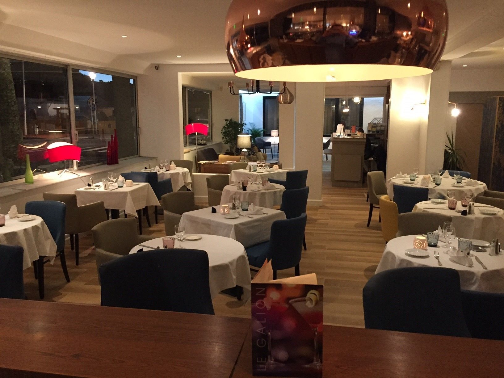 A restaurant with round tables, chairs, and a central chandelier.