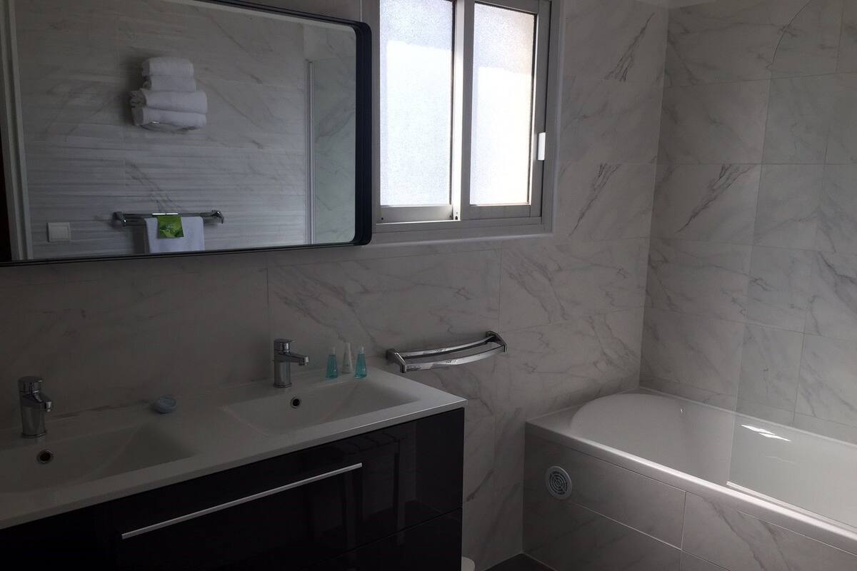 A modern bathroom with a large mirror, a sink with two faucets, a towel rack, and a toilet.