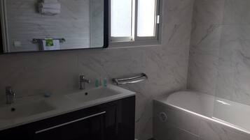 A modern bathroom with a large mirror, a sink with two faucets, a towel rack, and a toilet.