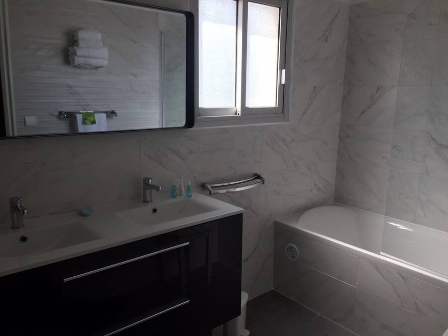 A modern bathroom with a large mirror, a sink with two faucets, a towel rack, and a toilet.