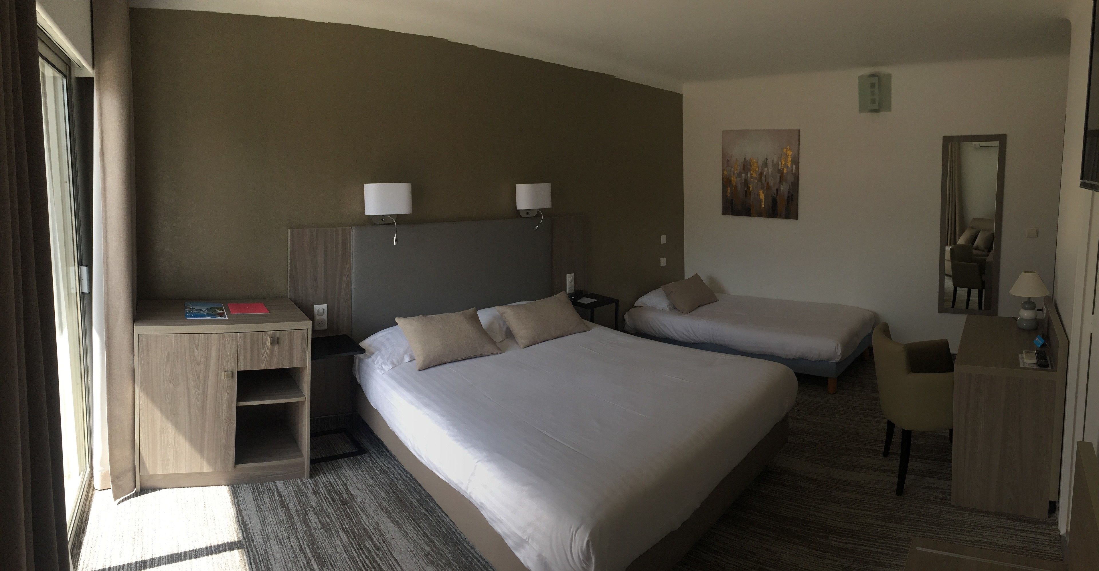 A hotel room with two beds, a desk, a chair, a small table, and a painting on the wall.