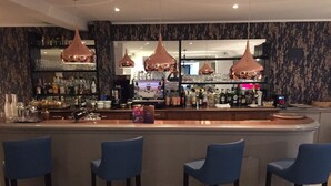 A bar area with three blue bar stools, a countertop with various bottles, and pendant lights. - Logis Hotel et Restaurant Le Galion Canet Plage (Canet-en-Roussillon)