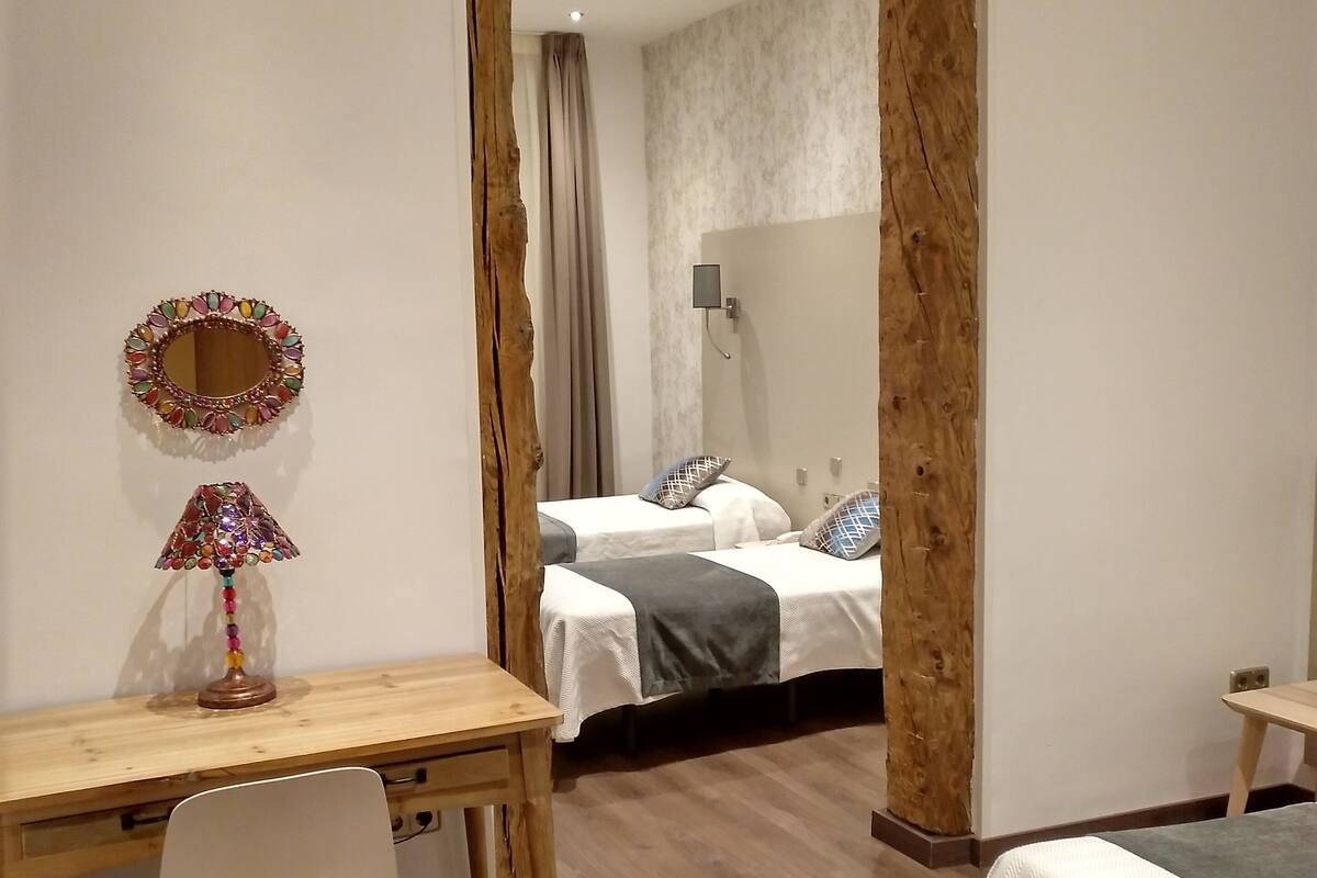 Quarto com escrivaninha de madeira, uma cadeira, cama com cobertor cinzento e espelho na parede.