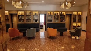 Un vestíbulo con piso de mármol, dos sofás y una mesa de centro. Hay estanterías con diversos objetos y una puerta que da a otra habitación.