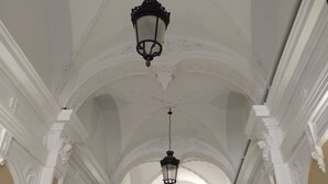 Un interior con techo alto, columnas blancas ornamentadas y candelabros negros colgantes.