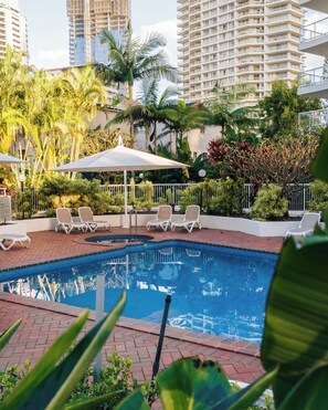 A swimming pool with lounge chairs, surrounded by palm trees and a white fence. - Crest Apartments (Main Beach)