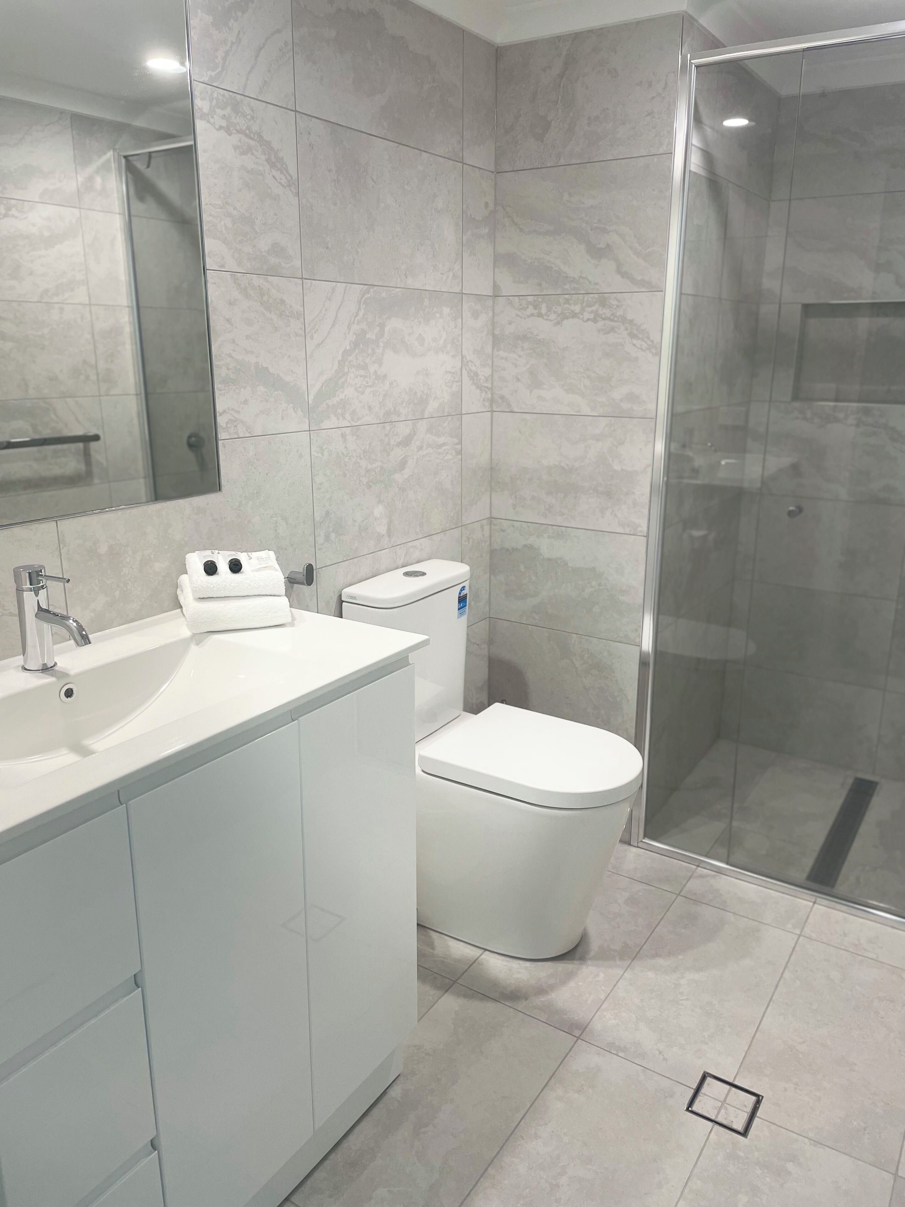 Een moderne badkamer met een wit wastafelmeubel, toilet en douchecabine.