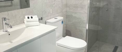 Een moderne badkamer met een wit wastafelmeubel, toilet en douchecabine.