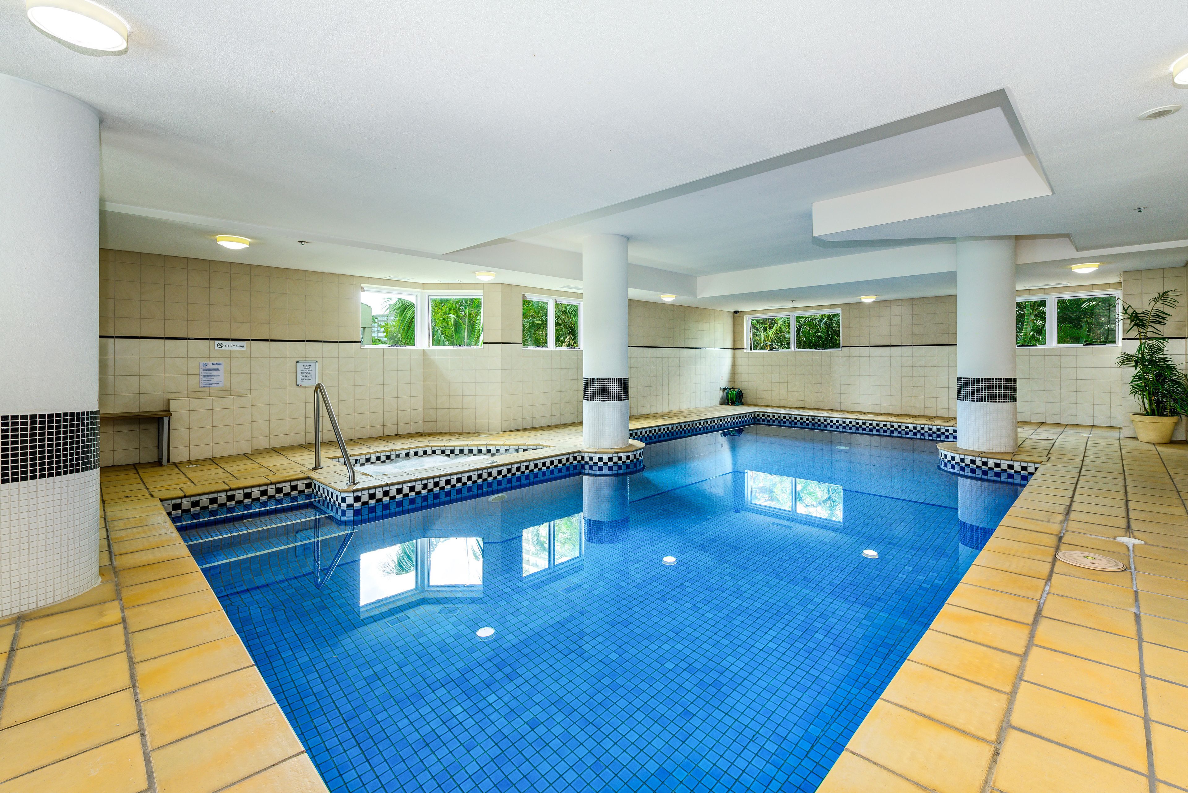 An indoor swimming pool with tiled walls and a tiled floor, surrounded by columns and windows.