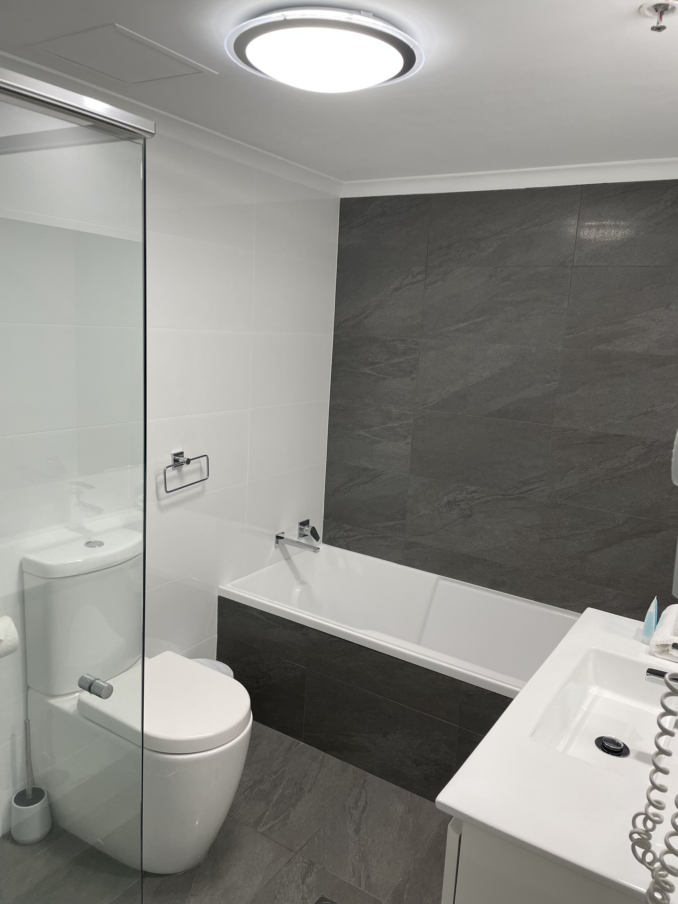 Ein modernes Badezimmer mit Duschkabine aus Glas, einer weißen Toilette, einer Badewanne und einem Waschbecken mit Handtuchhalter.