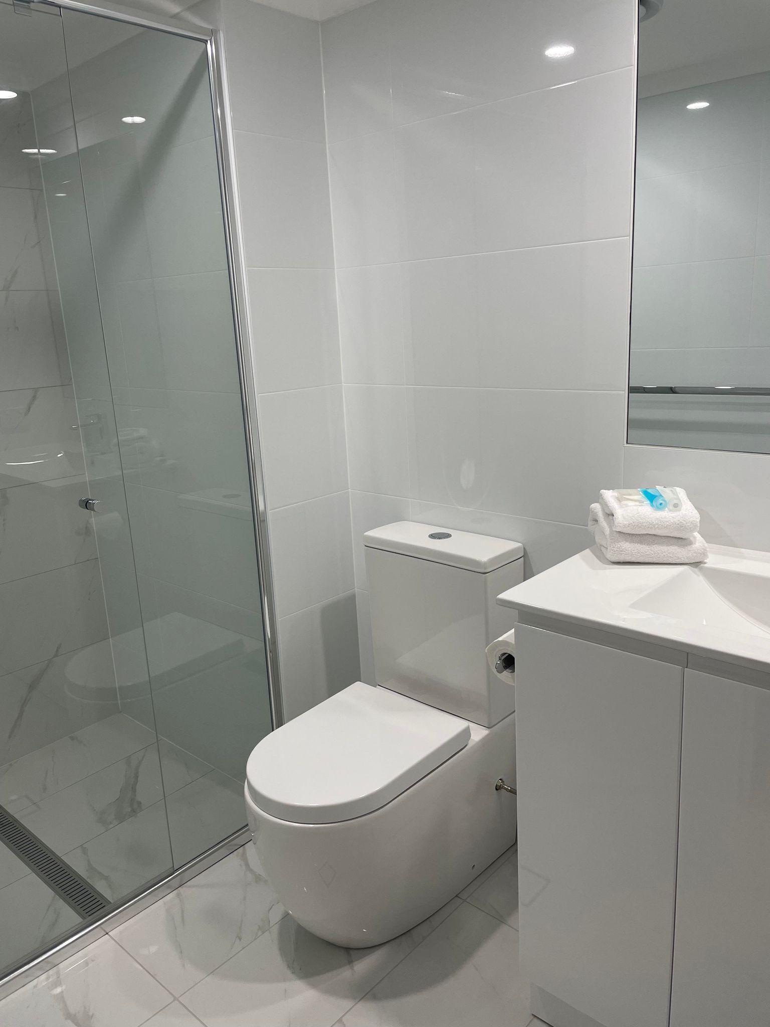 Une salle de bain moderne avec une douche à parois de verre, des toilettes blanches et un lavabo sur lequel est posée une serviette.