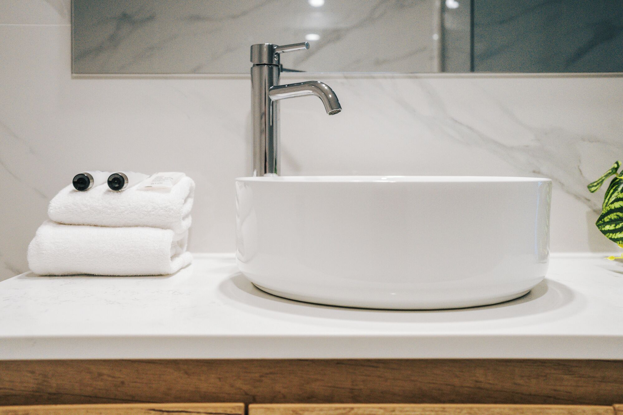 A bathroom with a white marble sink, a modern faucet, and a mirror above it.