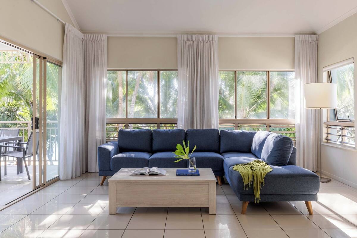 A modern living room with a sectional sofa, a coffee table, and large windows with curtains.