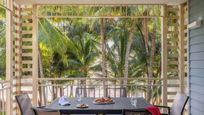 A covered outdoor dining area with a table and chairs, surrounded by a wooden lattice structure, overlooking a tropical garden with palm trees. - Mantra Amphora (Palm Cove)