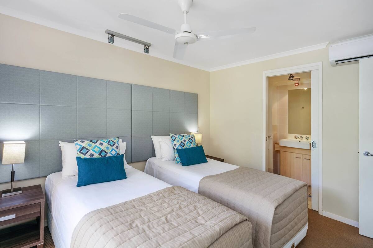 A hotel room with two beds, a ceiling fan, a nightstand, and a bathroom visible through an open door.