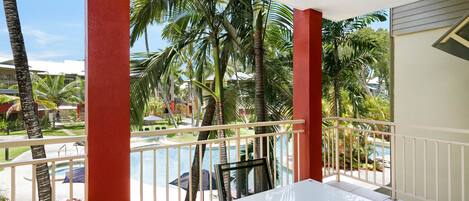A balcony with a white table and chairs, overlooking a pool and palm trees.