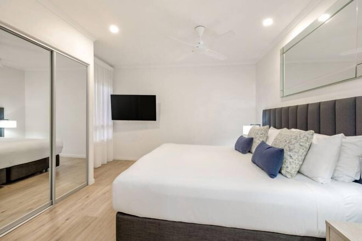 A modern bedroom with a bed, a ceiling fan, a flat-screen TV, and a large mirror.