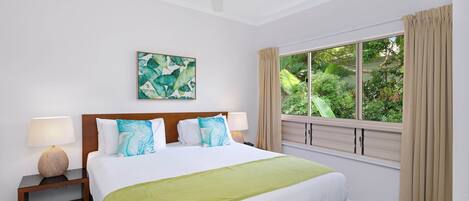 Une chambre d’hôtel avec un lit, deux tables de chevet, un ventilateur de plafond, une fenêtre avec des rideaux et une vue sur la verdure.