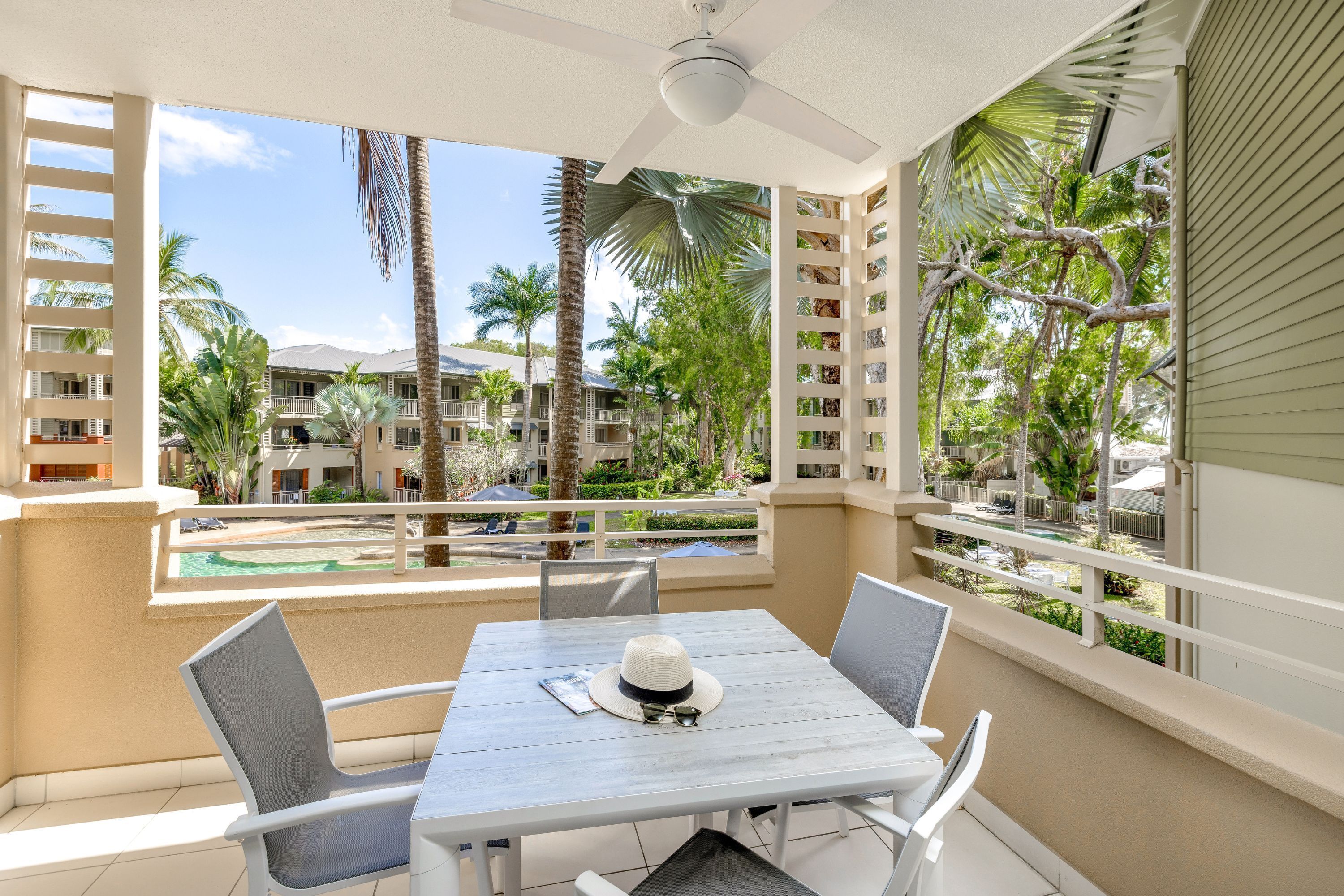 A balcony with a table and chairs, overlooking a pool and palm trees.