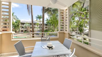 A balcony with a table and chairs, overlooking a pool and palm trees.