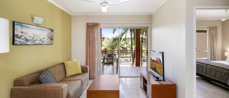 A modern living room with a sofa, coffee table, TV, and a balcony with a view of palm trees.