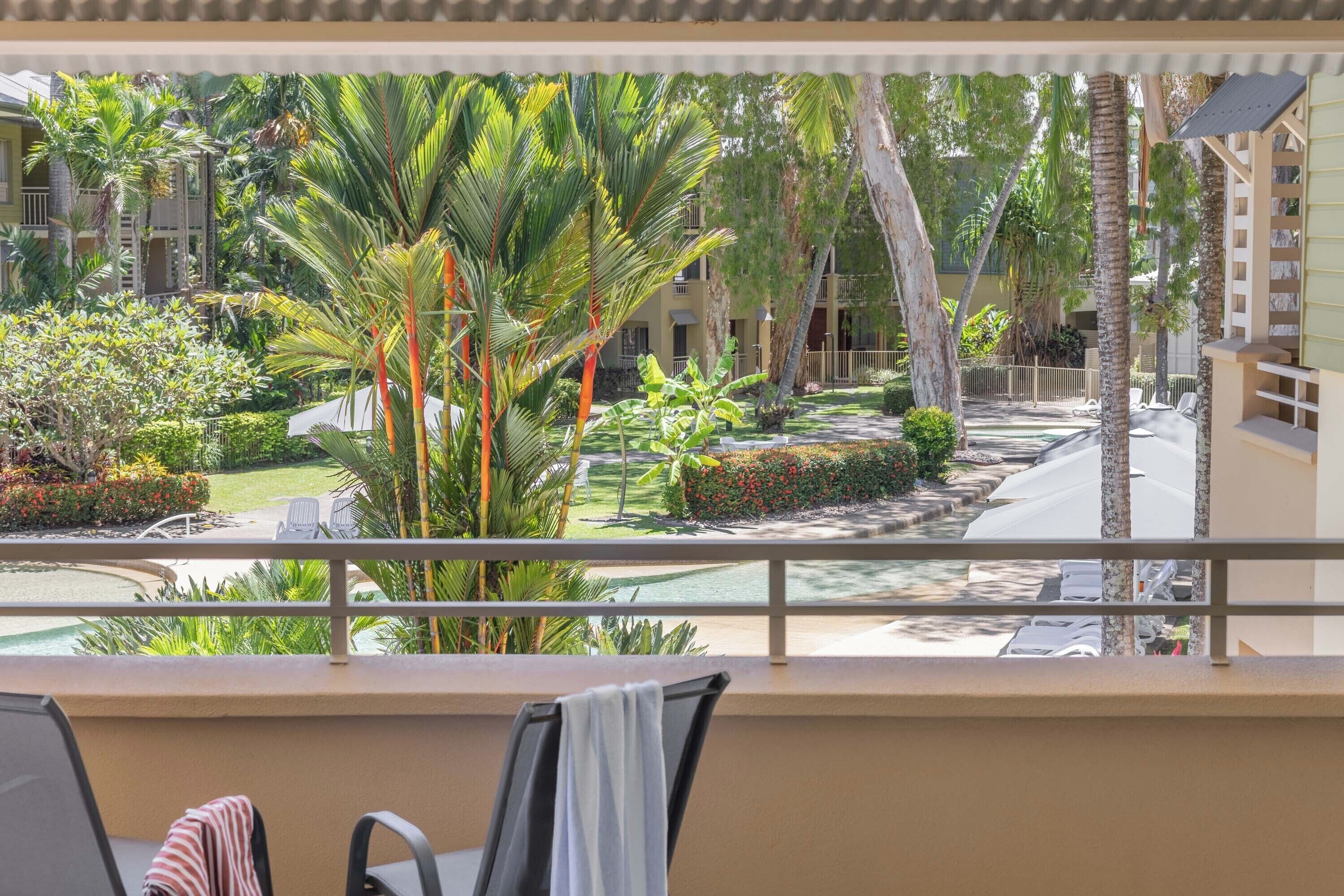 A balcony with a view of a landscaped garden, including palm trees and a pool.
