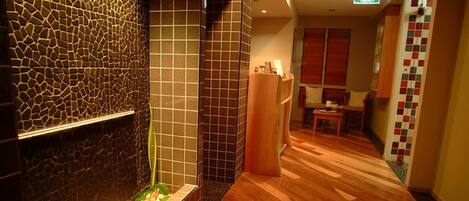 A hotel corridor with a stone wall, wooden flooring, and a seating area with a table and chairs.