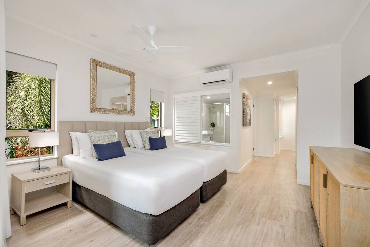 A modern bedroom with a large bed, bedside tables, a ceiling fan, and a TV.