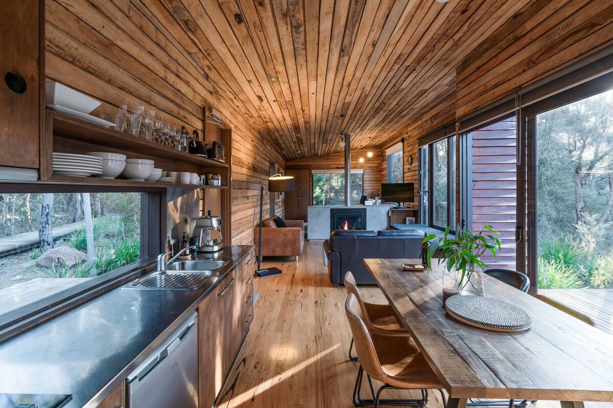 Cocina moderna con vigas de madera, electrodomésticos de acero inoxidable y un amplio ventanal con vistas a un jardín.